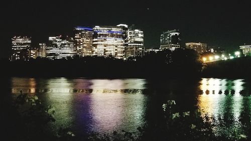 Illuminated buildings by river against sky at night