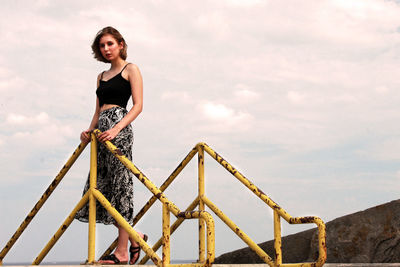 Portrait of woman standing on railing against sky