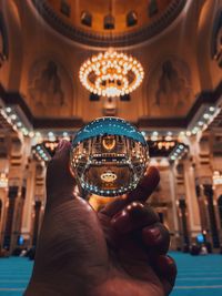 Cropped hand holding crystal ball against lighting equipment