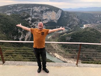 Full length of mid adult man with arms outstretched standing on observation point against mountains