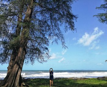 Rear view of mature woman with arms raised standing at beach against sky