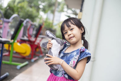 Portrait of cute girl holding stuffed toy while standing outdoors