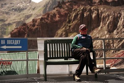 Full length portrait of man sitting on railing
