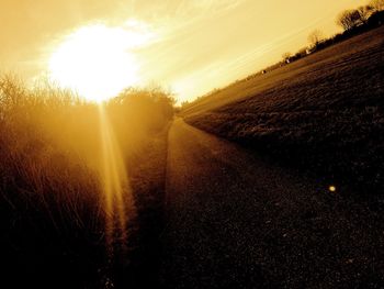 Road amidst agricultural field against sky during sunset