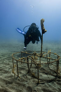 Woman wearing diving equipment by metal on ocean floor in sea