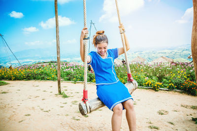Full length of smiling girl on swing against sky