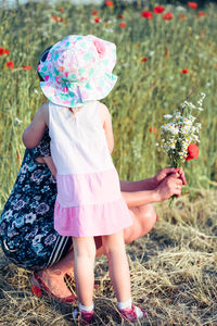 Girl standing by mother holding flowers on grass