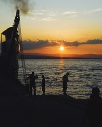 Silhouette people on beach by sea against sky during sunset