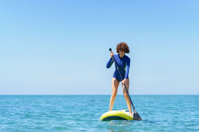 Rear view of woman jumping in sea against clear sky