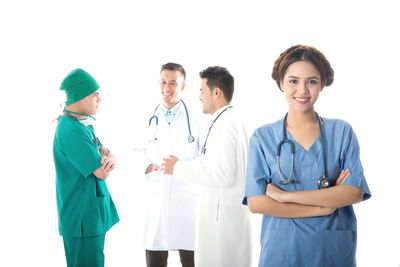 Portrait of female doctor while coworkers discussing against white background