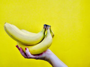 Close-up of hand holding fruit against yellow background