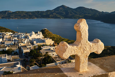 Christian cross and plaka village on milos island over red geranium flowers on sunset in greece