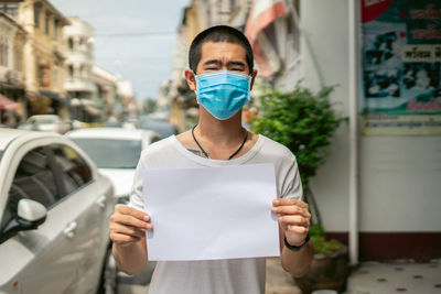 Portrait of young man holding paper while standing outdoors