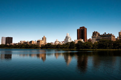 Scenic view of river by buildings against clear blue sky