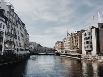 Bridge over river by buildings in city against sky