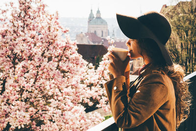 Beautiful woman in brown hat drinking coffee at outdoor cafe with amazing view of spring prague.
