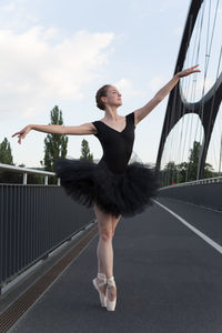 Female ballet dancer dancing on bridge against sky