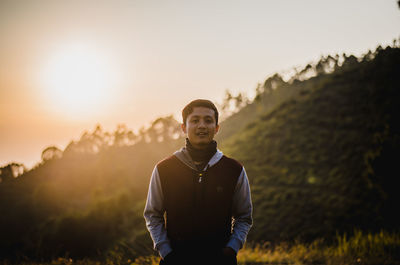 Portrait of young man standing on field during sunset