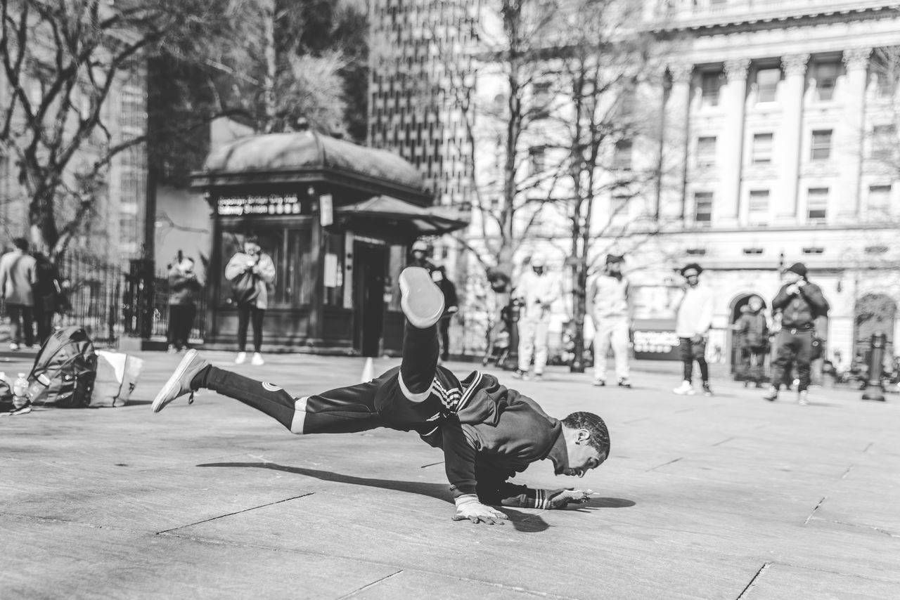 real people, lifestyles, men, architecture, city, full length, one person, incidental people, leisure activity, built structure, building exterior, tree, day, casual clothing, focus on foreground, balance, nature, street, outdoors, handstand