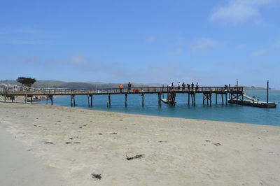 People on pier over sea against sky