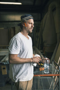 Carpenter holding water bottle and disposable glass in workshop