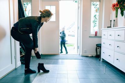 Woman wearing shoes while daughter walking out of doorway