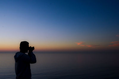 Man photographing sea against sky during sunset