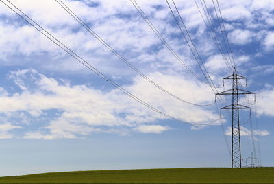 Electricity pylon on field against cloudy sky