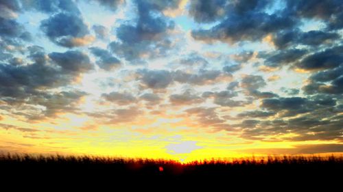 Scenic view of landscape against cloudy sky at sunset