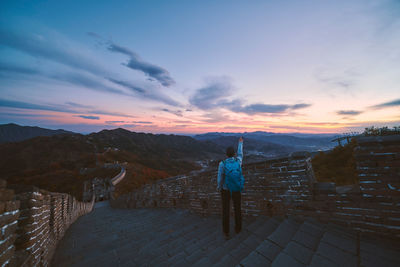 Rear view of mature man with backpack standing on steps against sky during sunset