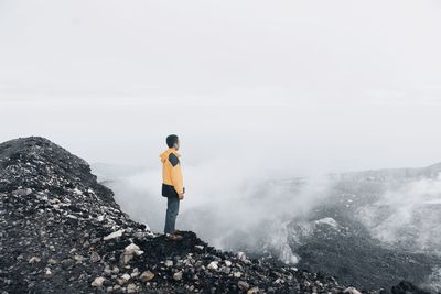 Rear view of man standing on rock against clear sky