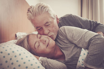 Senior man kissing woman on bed at home