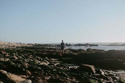 Rear view of man standing on rock against sea at beach