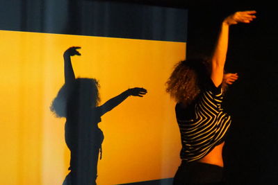 Rear view of woman with arms raised standing against wall