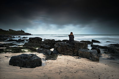 Girl in black looking out to sea sitting on rocks