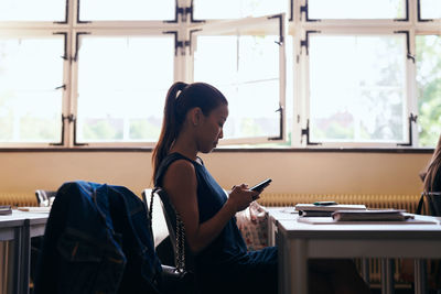 Young woman using mobile phone while sitting on table