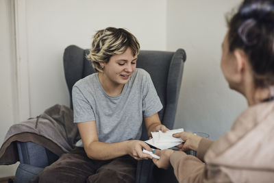 Smiling female students taking sanitary pads and tampons from non-binary counselor in school office