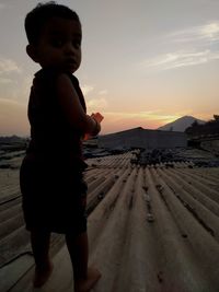 Boy standing on beach against sky during sunset