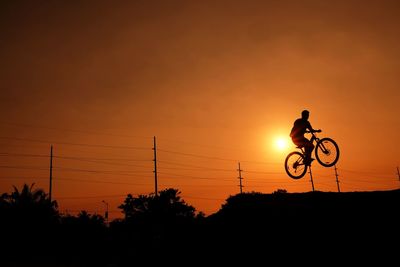 Silhouette person riding bicycle against sky during sunset