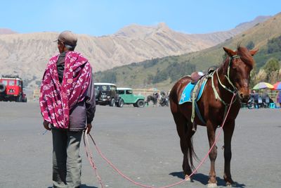 Rear view of man standing with horse on road against mountains