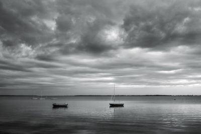 Sailboats in sea against cloudy sky