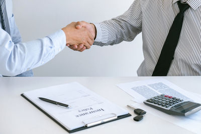 Midsection of agent giving handshake to customer in office