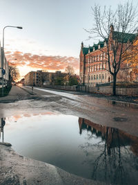 Canal by buildings against sky during sunset in city