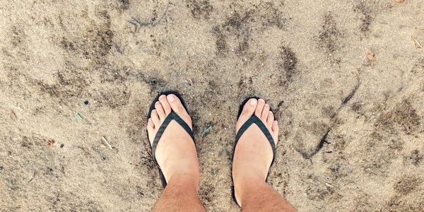 Low section of man wearing flip flops standing on sand