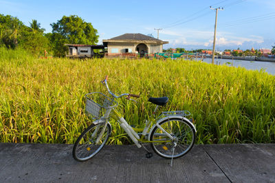 Bicycle parked on field by house against sky