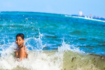 Waves splashing on shirtless boy swimming in sea