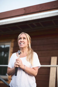 Angry woman clenching teeth while holding hammer outside house being renovated