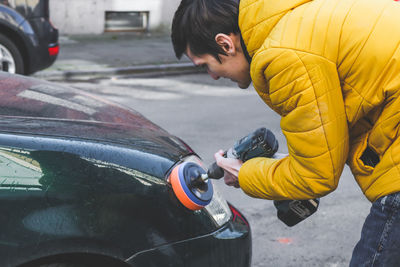 The hands of a  guy are drilling a drill with a disk with a sponge and polishing the headlight