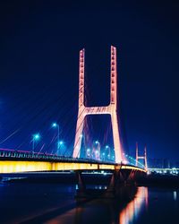 Illuminated bridge over river against sky at night