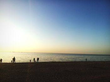 Silhouette people standing on beach against clear sky